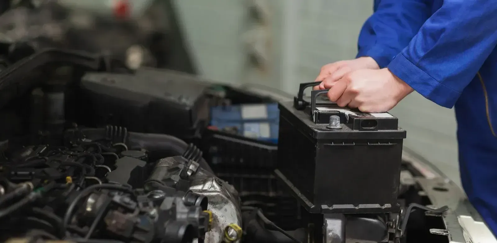 A mechanic is working on a car battery in a garage.