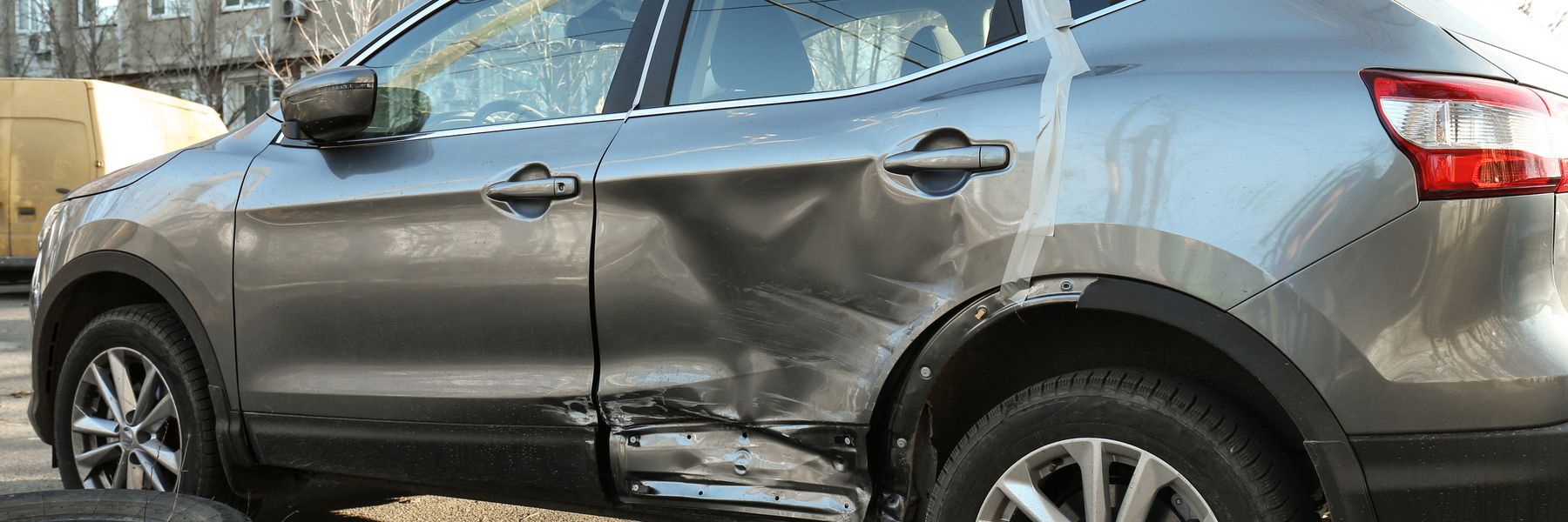 A gray car with significant damage to its side panels. The car appears to have been involved in a collision.