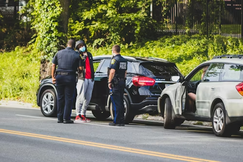 Police officers talking with a driver beside a black SUV on a roadside beside a silver car.