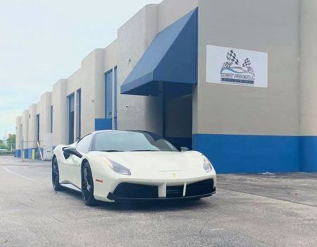 A white sports car is parked in front of a building with a blue awning.