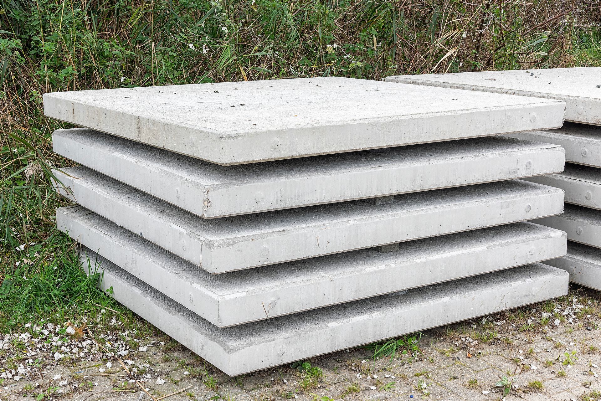 Square concrete slabs lie outside in front of a piece of dune ground. Square concrete slabs lie outside in front of a piece of dune ground.