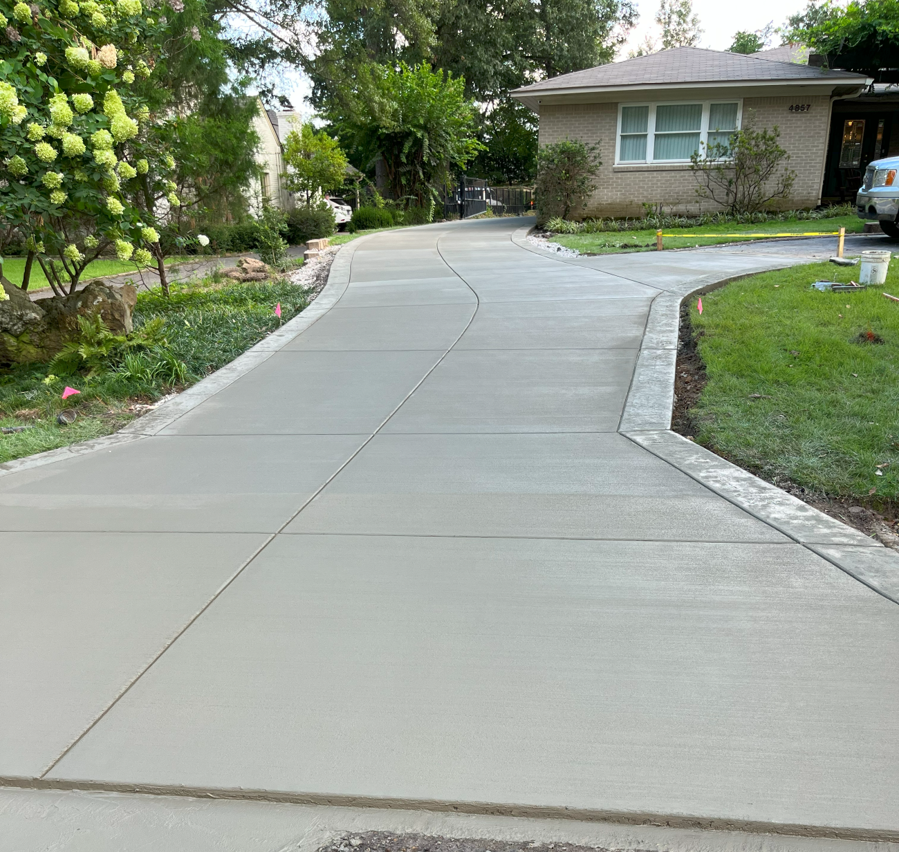Newly poured concrete driveway curves towards a light-colored brick house; green landscaping borders the driveway.
