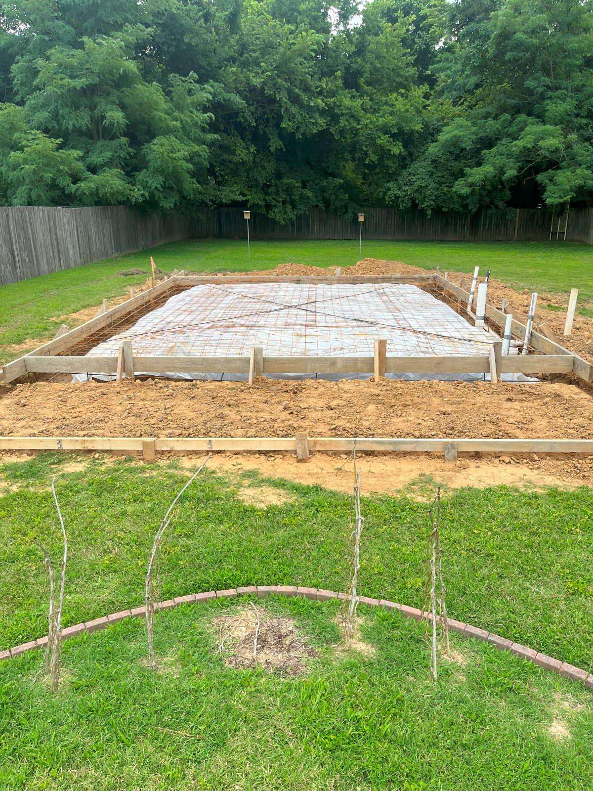 Concrete foundation, surrounded by wooden forms and dirt, set in a grassy yard.