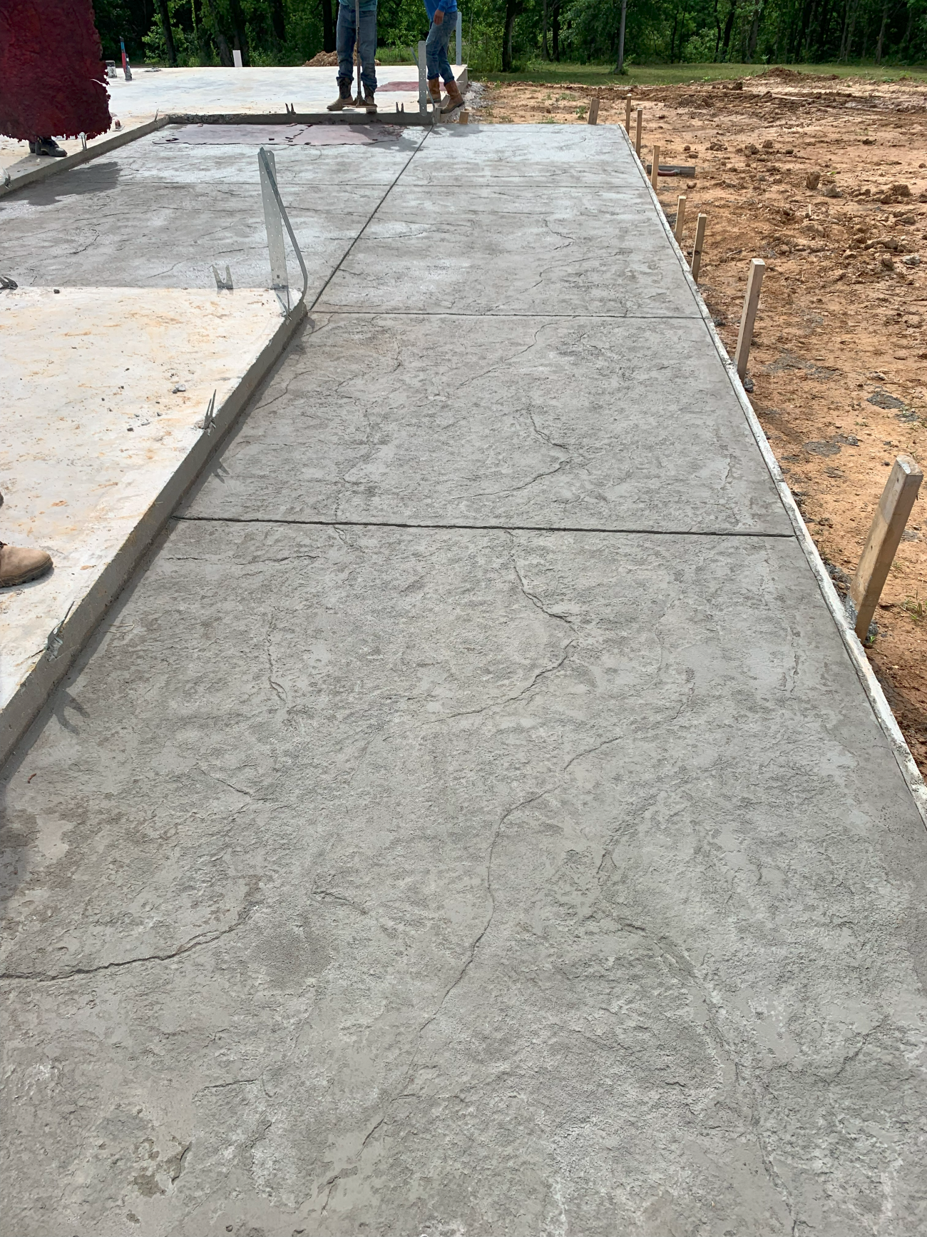 Freshly poured concrete walkway, divided into sections with control joints, near a construction site.