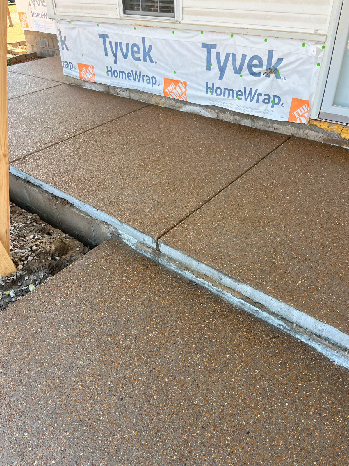 Concrete sidewalk, newly poured, next to a building under construction, with Tyvek wrap visible.