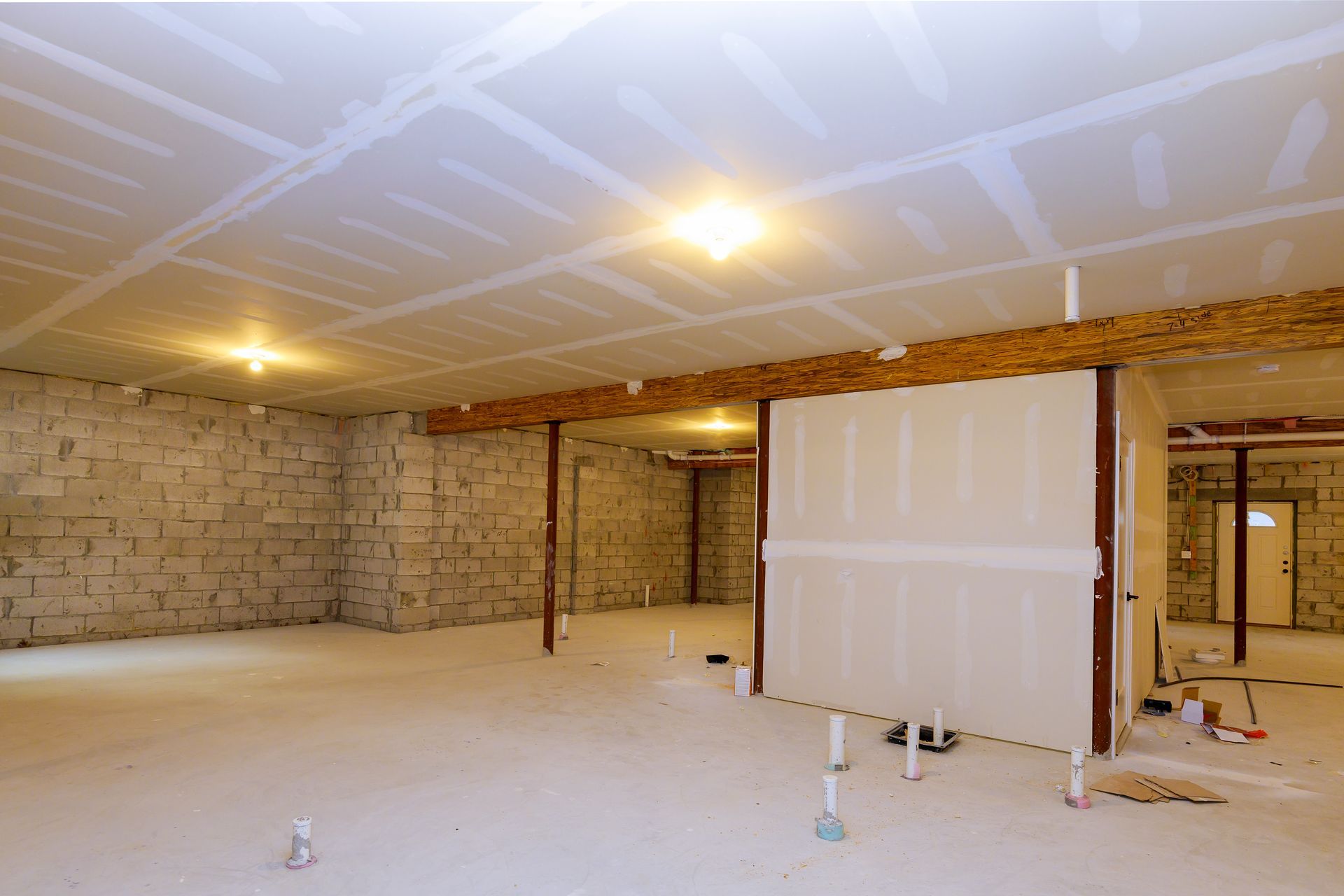 Basement renovation: unfinished drywall on walls and ceiling, exposed beams, bare concrete block walls.