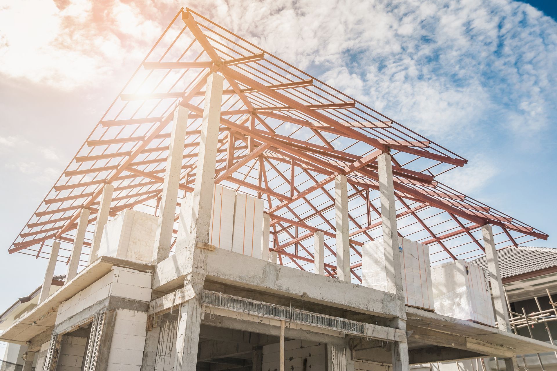 Construction of a two-story home with exposed roof trusses, blue sky, and bright sunlight.