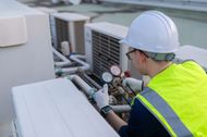 HVAC technician in hard hat and vest checks gauges on rooftop air conditioning units.