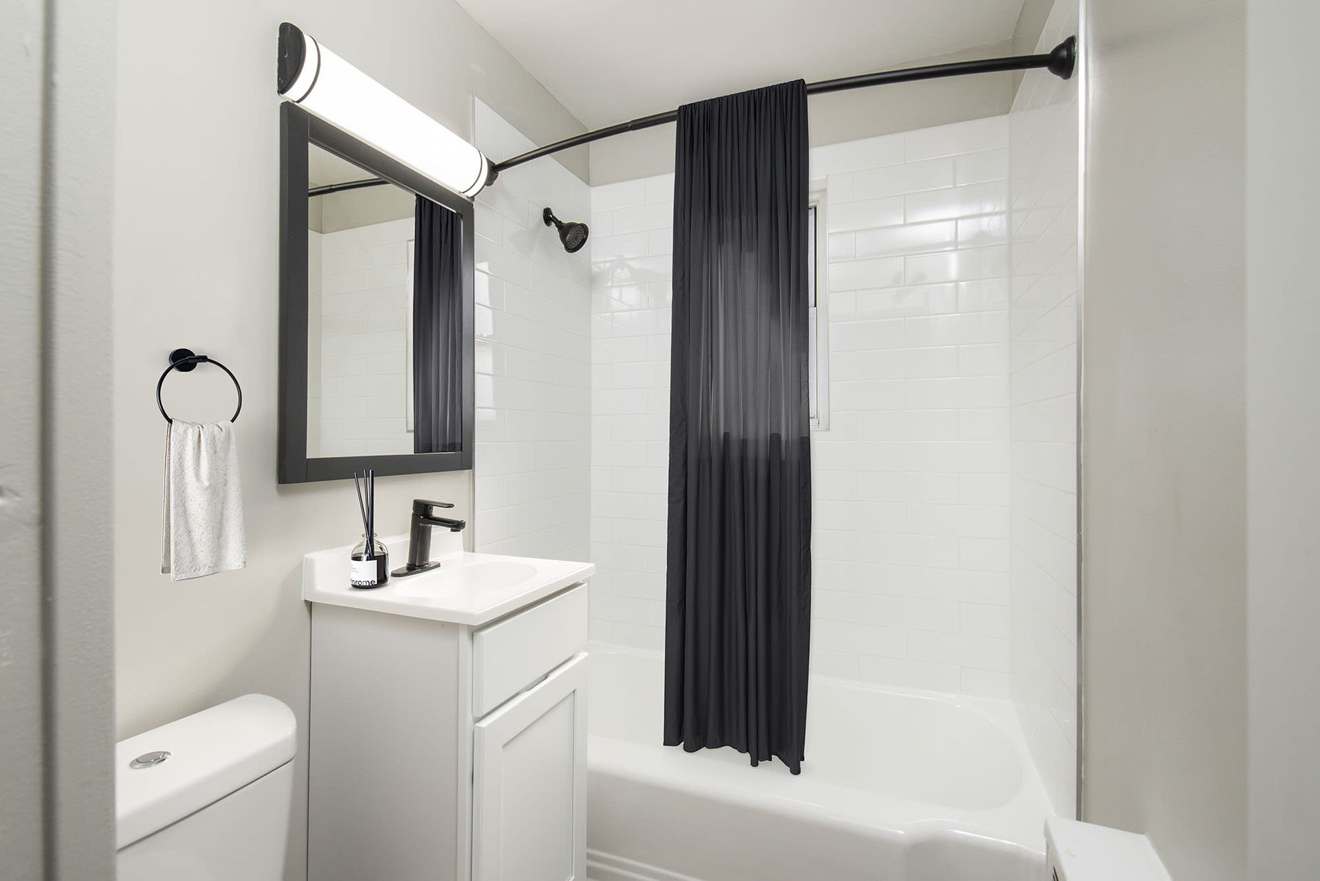 White bathroom with sink, vanity, toilet, and a dark shower curtain.