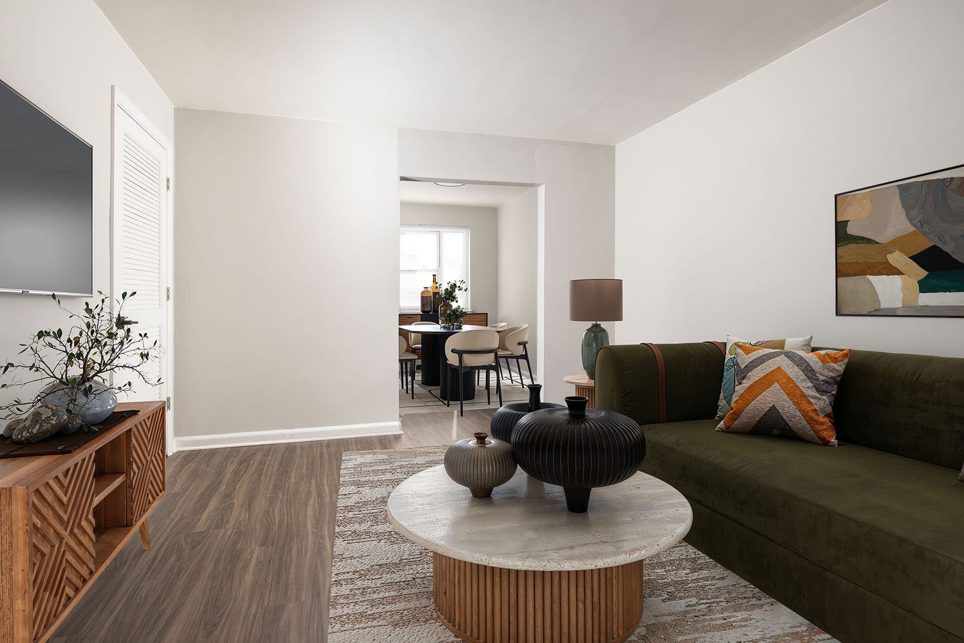 Living room in an apartment with an olive-green sofa, round marble coffee table, and wall-mounted TV.