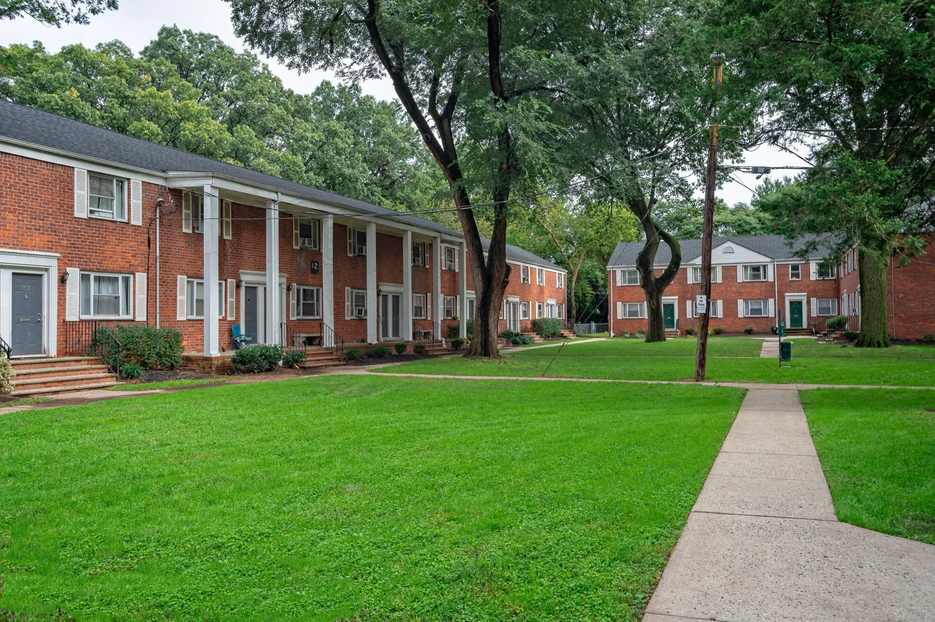 Exterior view of a brick apartment community with lawns, walkways, and mature trees.