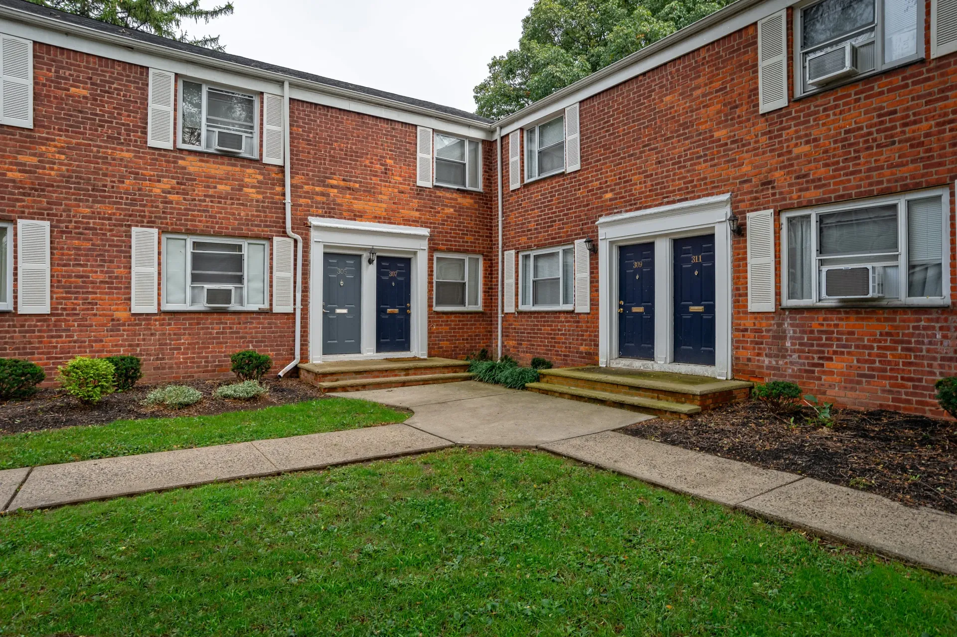 Brick exterior of a multi-unit apartment building with blue doors and small steps.
