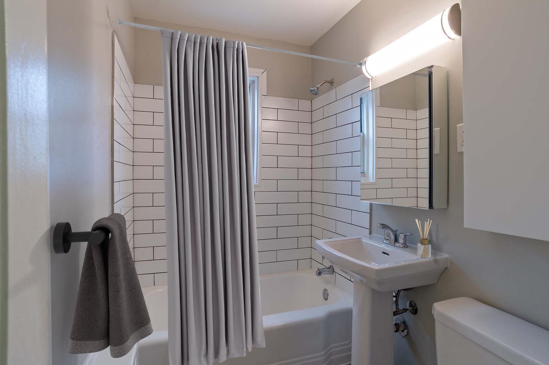 Apartment bathroom with a shower curtain, white subway-tile walls, pedestal sink, and mirror.