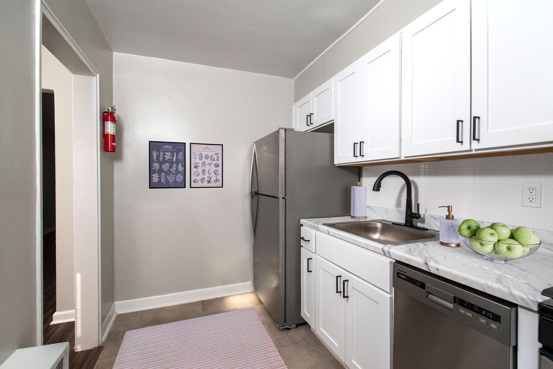 Bright apartment kitchen with white cabinets, stainless steel fridge, sink, and dishwasher.