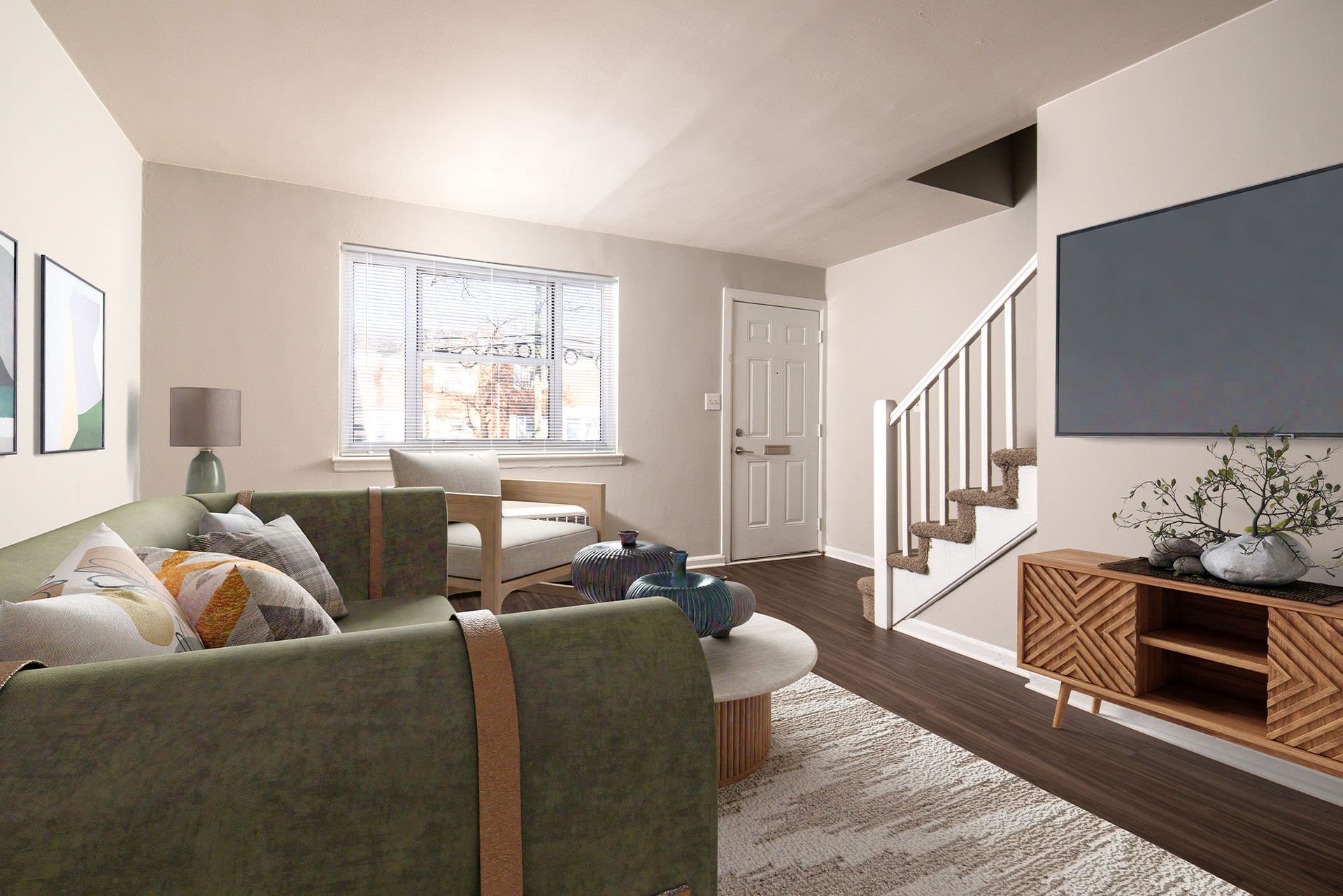 Living room in an apartment with a green sofa, wooden coffee table, stairs, and front door.