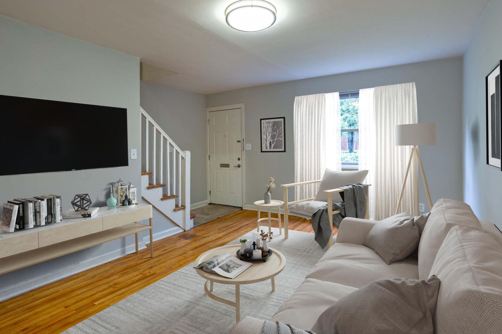 Living room in an apartment with a beige sofa, round coffee table, TV on wall, and staircase.