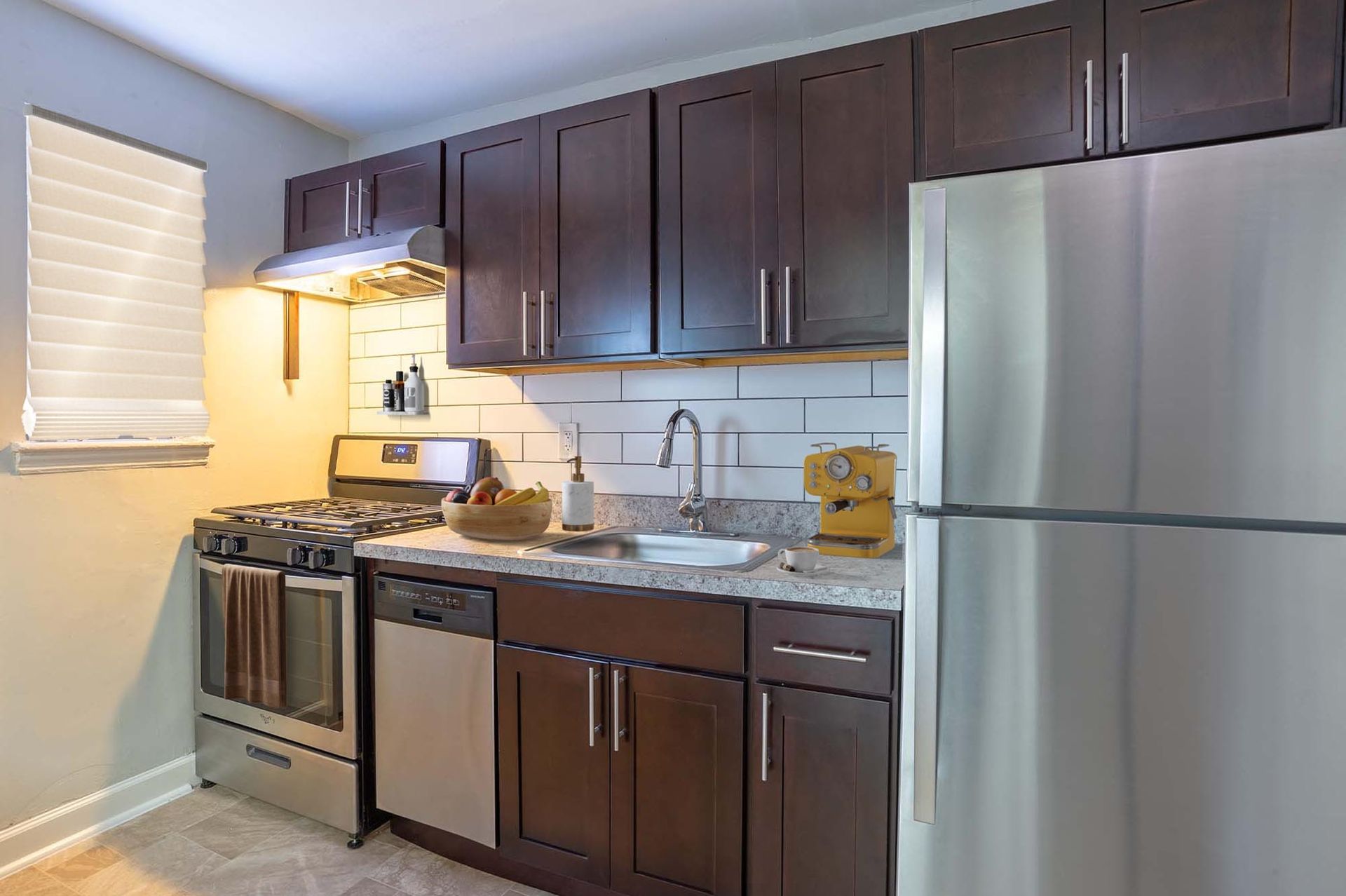 Modern apartment kitchen with dark cabinets, stainless steel appliances, and a white subway tile backsplash.