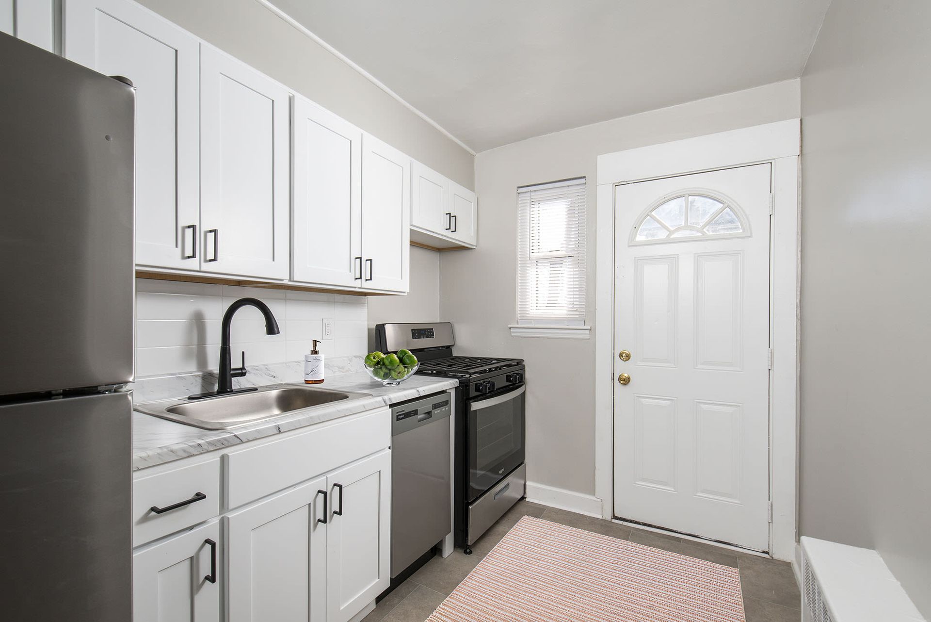 Bright kitchen in an apartment with white cabinets, a black faucet, and stainless steel appliances.