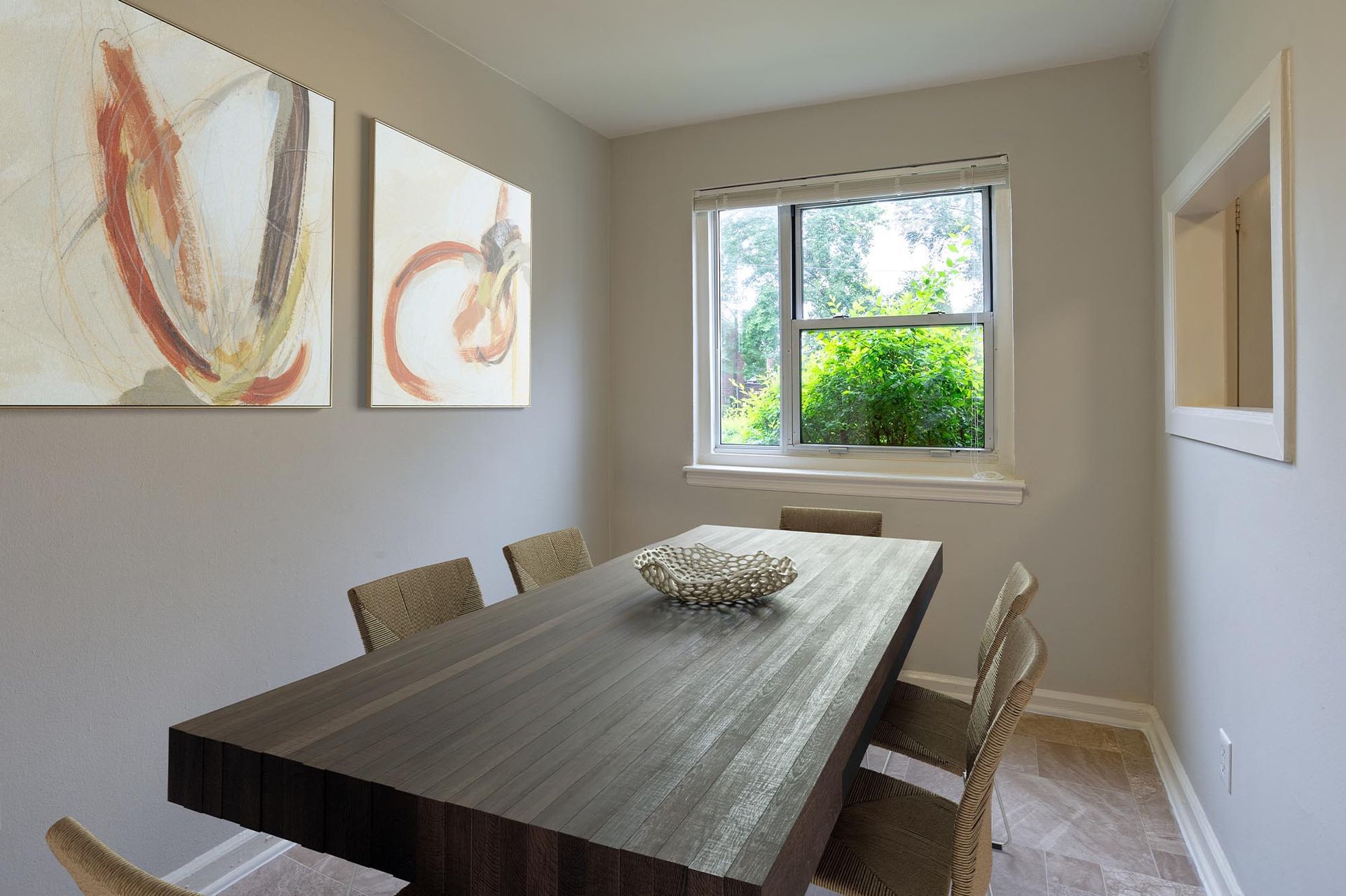 Dining room with a dark rectangular wooden table, wicker chairs, and a window view of greenery.