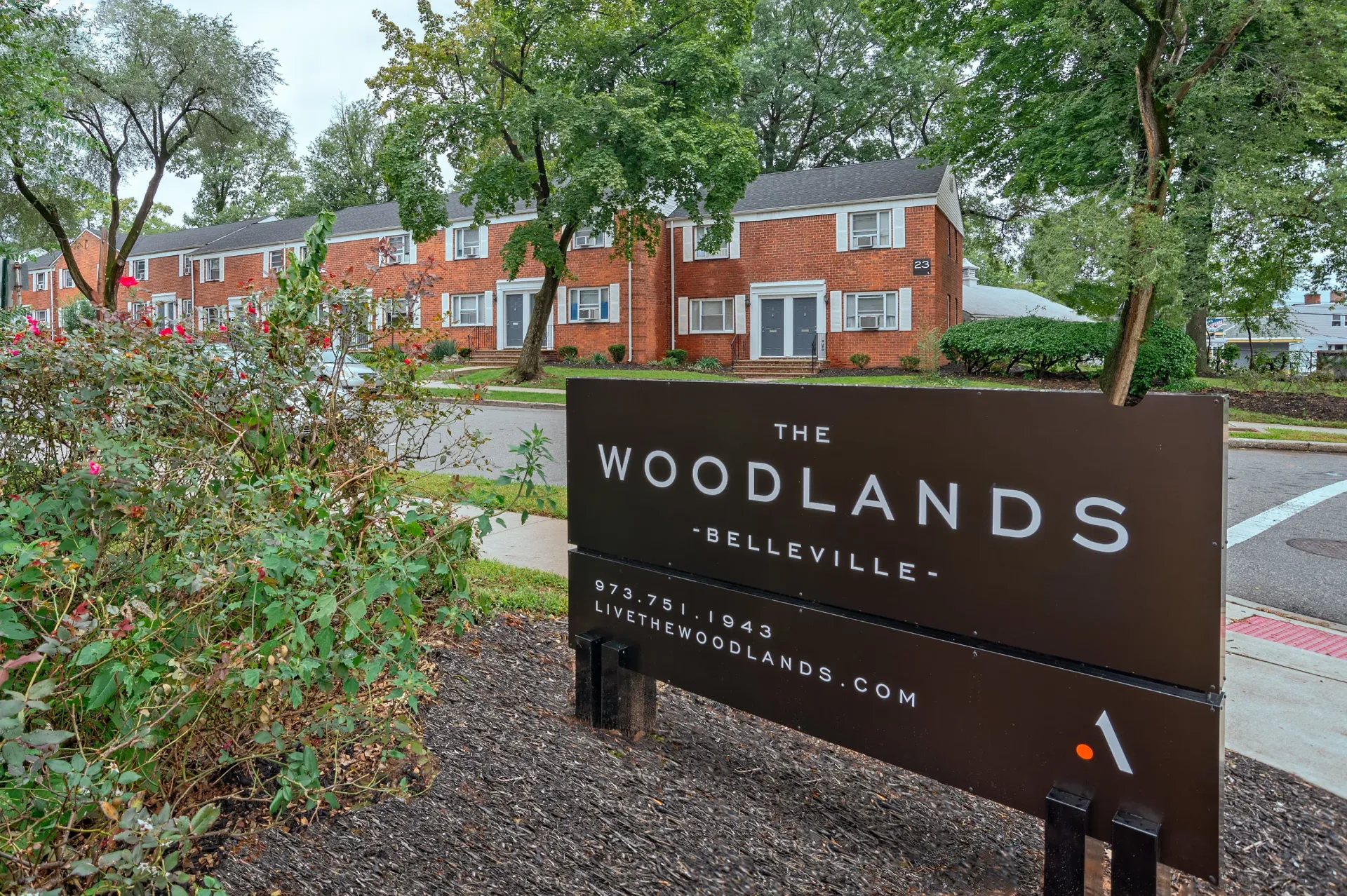 Exterior view of The Woodlands Belleville sign with brick apartment buildings behind.