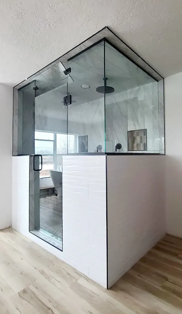 Modern shower enclosure with glass walls and white tiled base. Black fixtures.