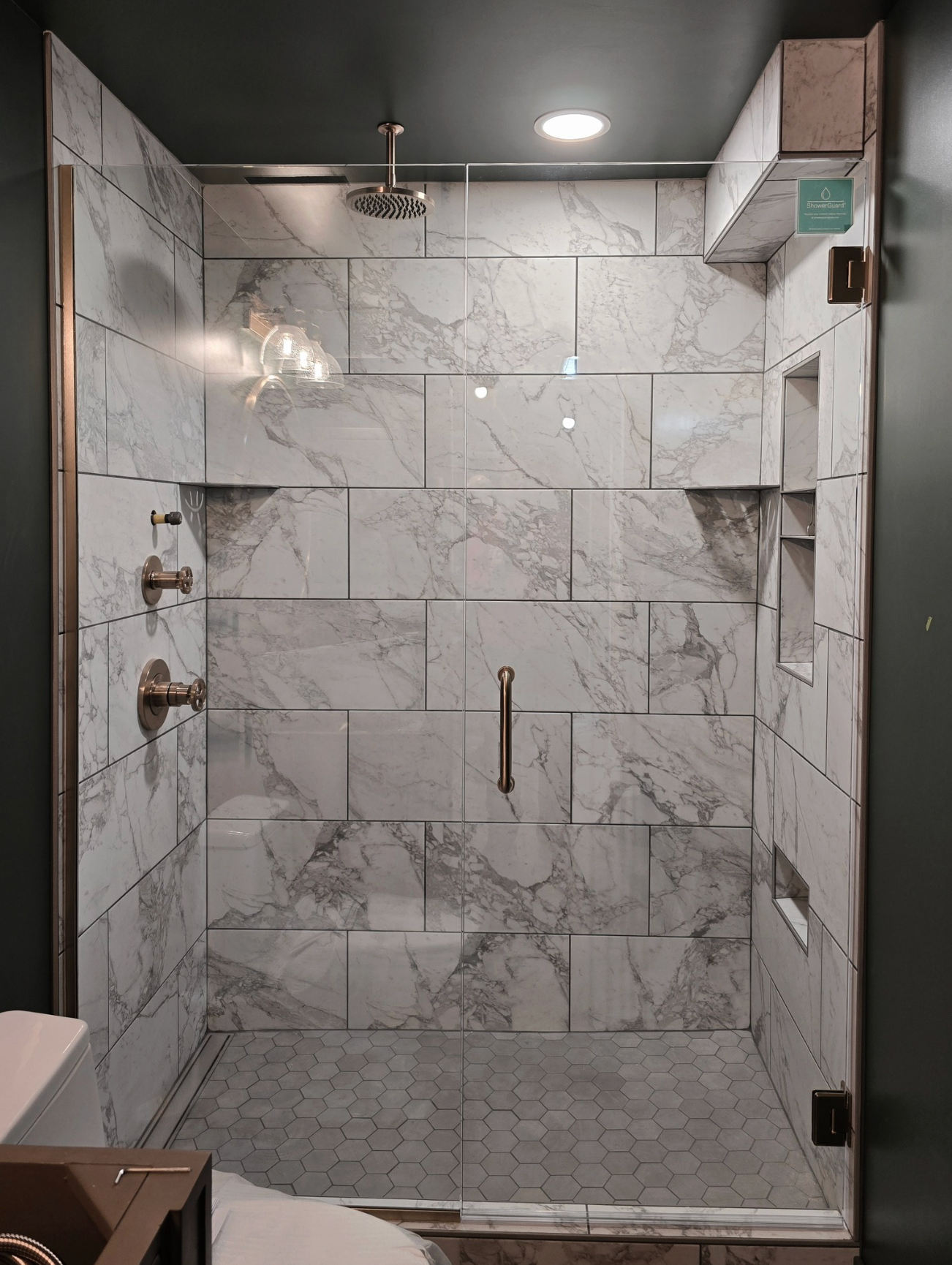 Shower with white marble-like tile, glass doors, and bronze fixtures.