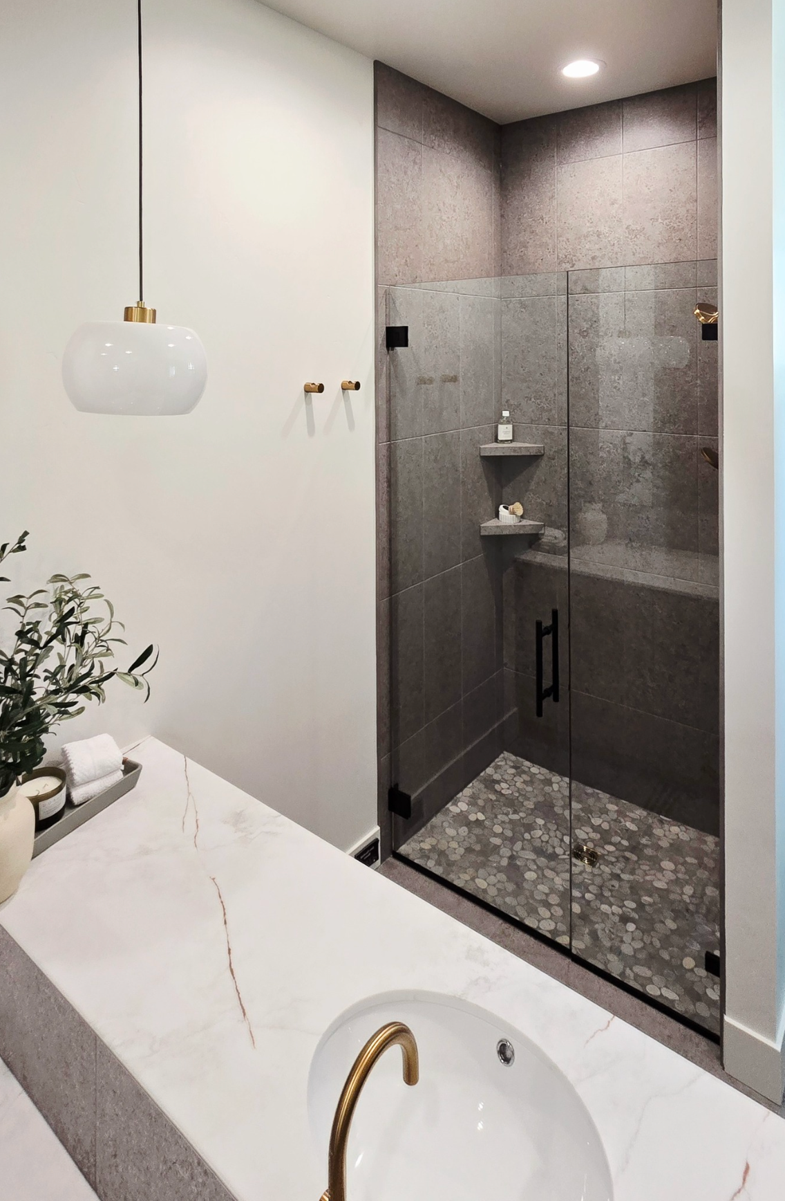 Modern bathroom with marble countertops, glass shower, and gold fixtures.