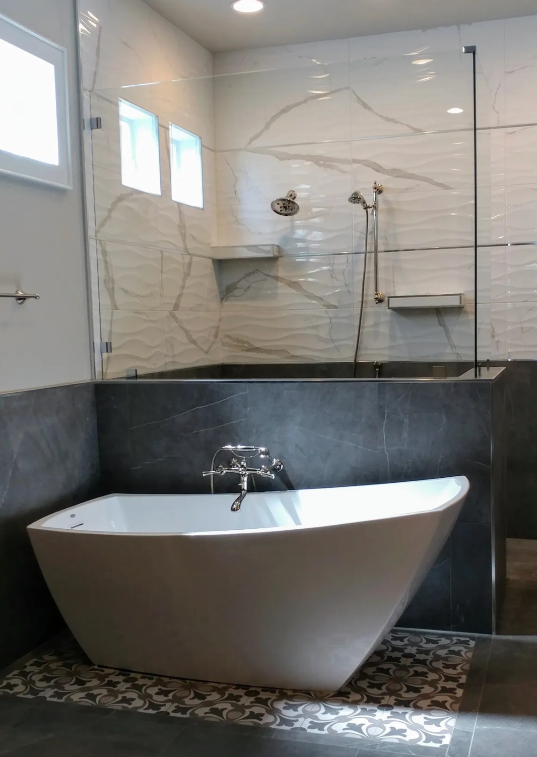 Modern bathroom with white tub, marble tile, and glass shower enclosure.