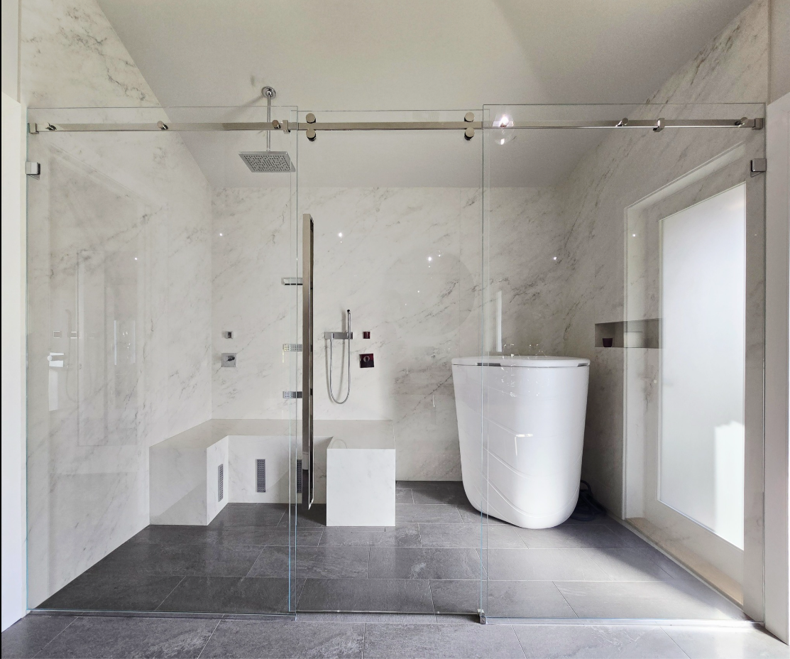 Modern bathroom with glass shower enclosure, a bathtub, and marble walls.