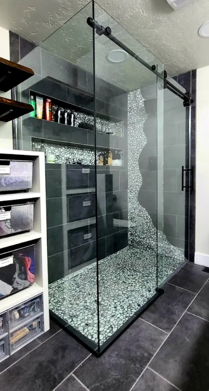 Modern shower with clear glass walls and pebble flooring. Black trim and sliding door.