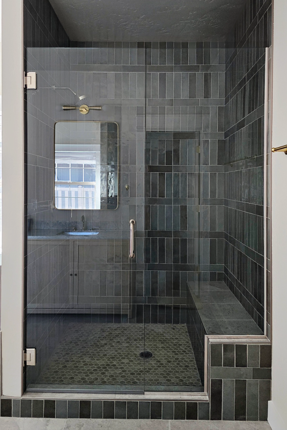 Modern bathroom with gray tiled shower, glass door, bench, and vanity.