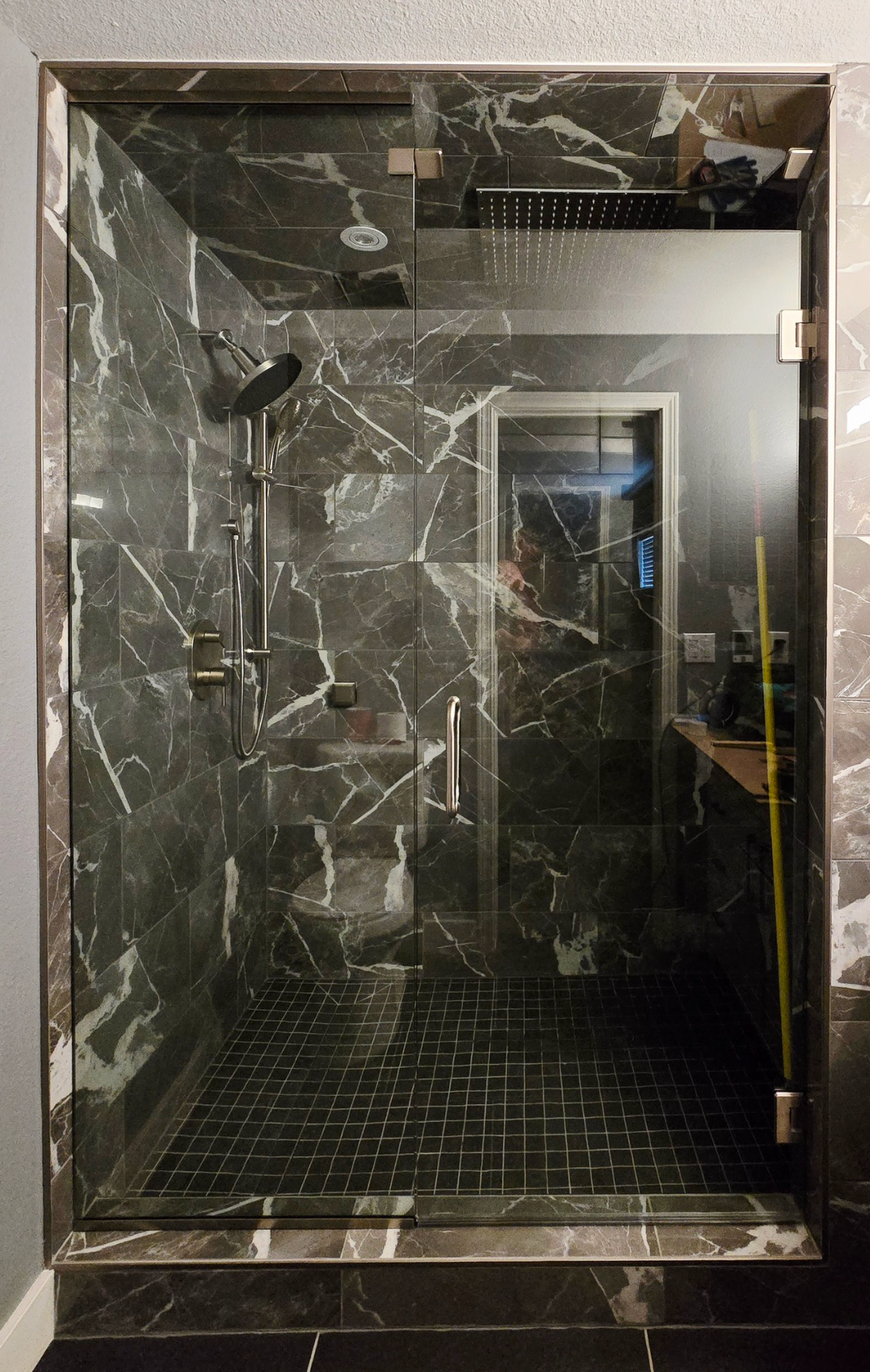 Black marble shower with glass door and rain showerhead.