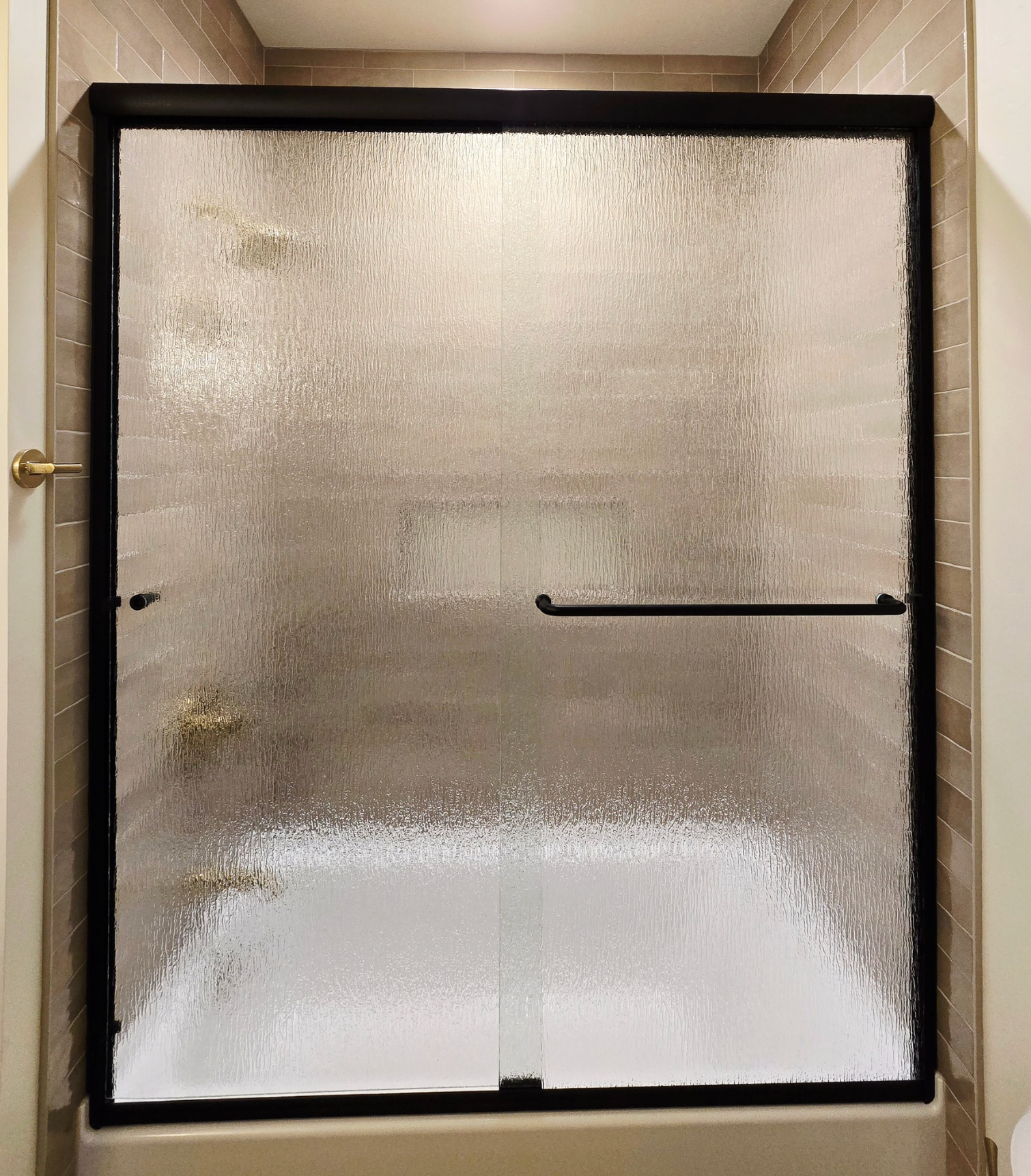Textured glass shower door with black frame, gold fixtures.