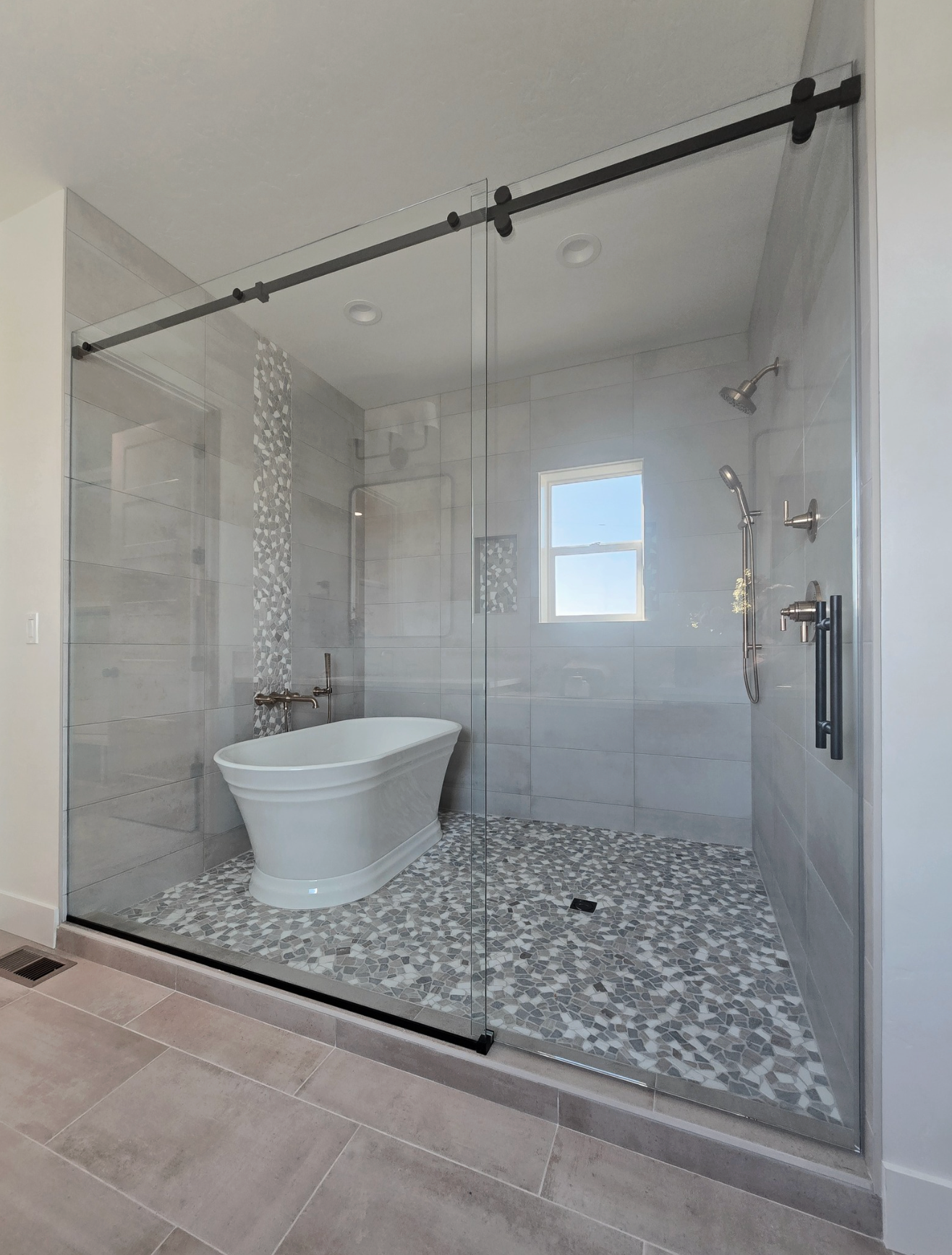 Modern bathroom with a glass-enclosed shower, freestanding tub, and light gray tiled walls.