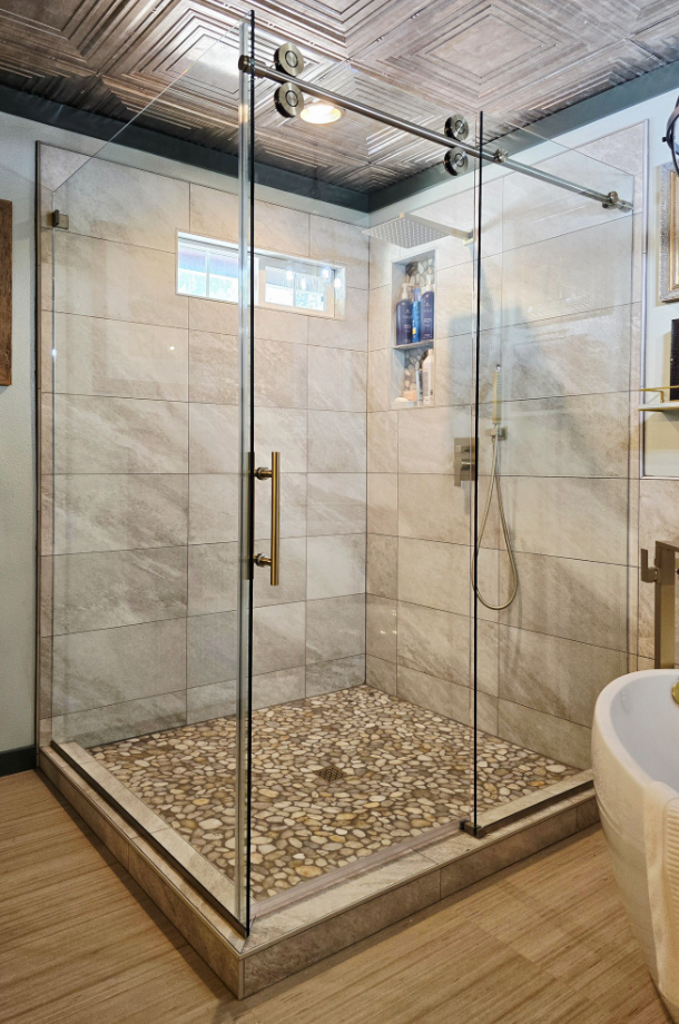 Glass-enclosed walk-in shower with pebble floor and beige tiled walls in a modern bathroom