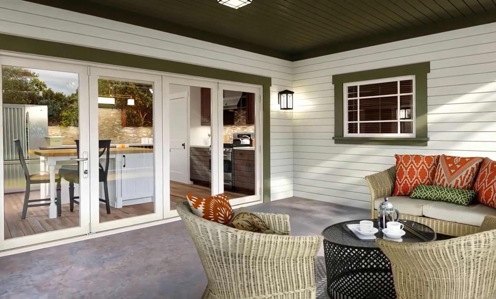 A cozy outdoor patio with wicker furniture, set against a white-walled house with green trim and glass sliding doors.