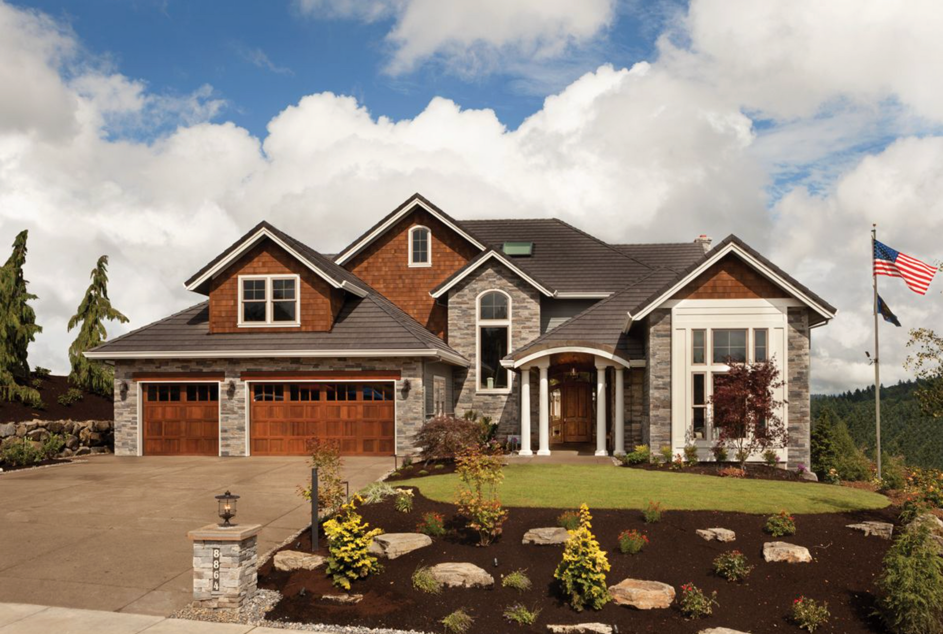A modern multi-story suburban home with a gray stone facade, cedar shingles, and an attached two-car garage.