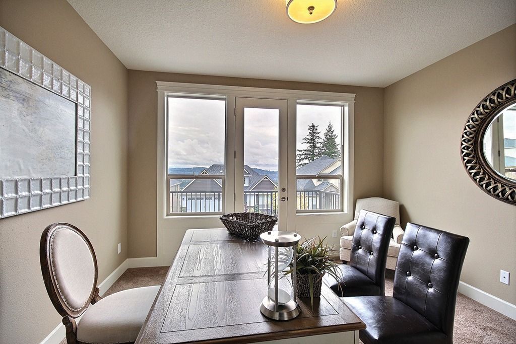 Dining room with wooden table, dark leather chairs, large windows, and a decorative mirror.