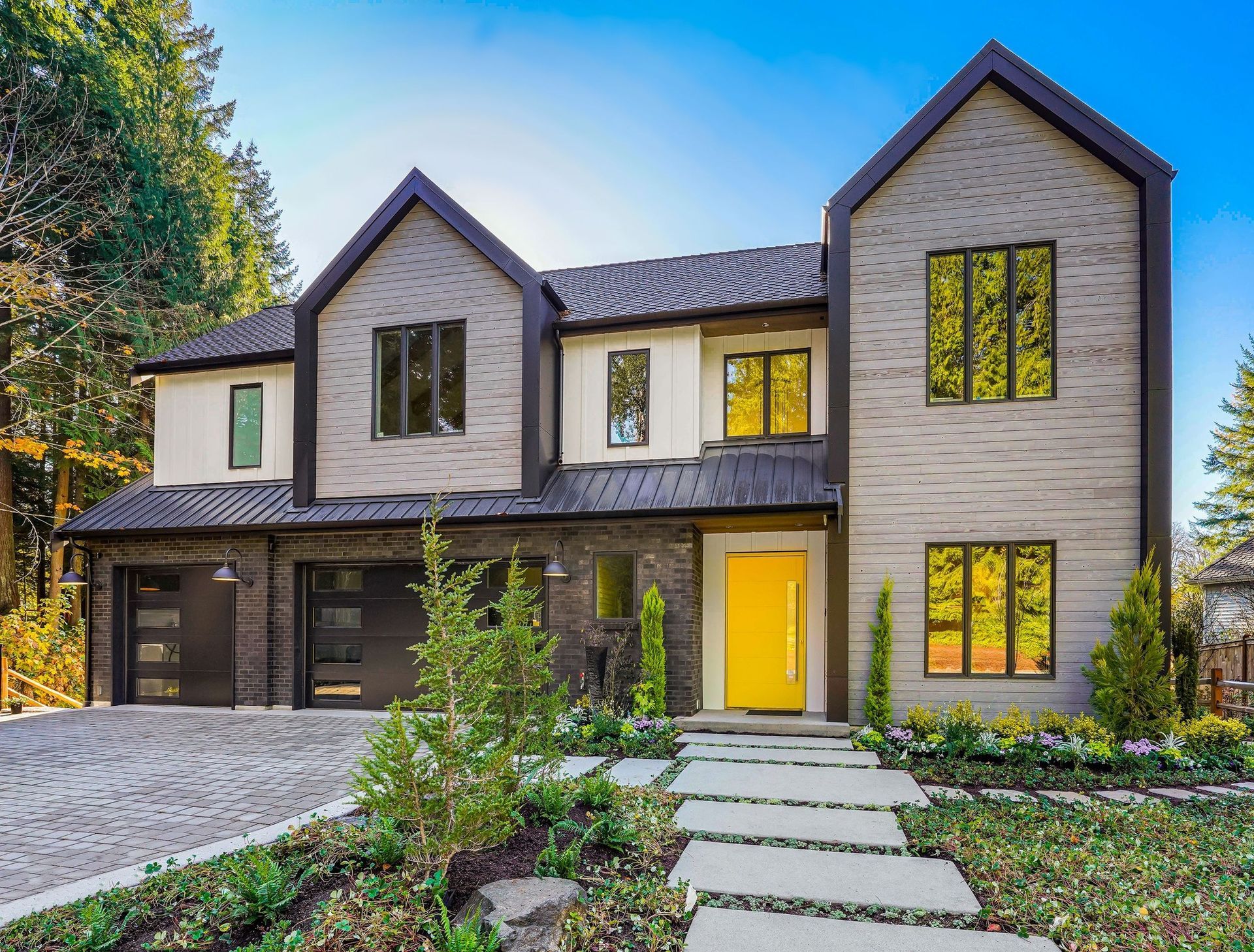 Modern two-story house with gray and tan siding, yellow door, black trim, and stone pathway.