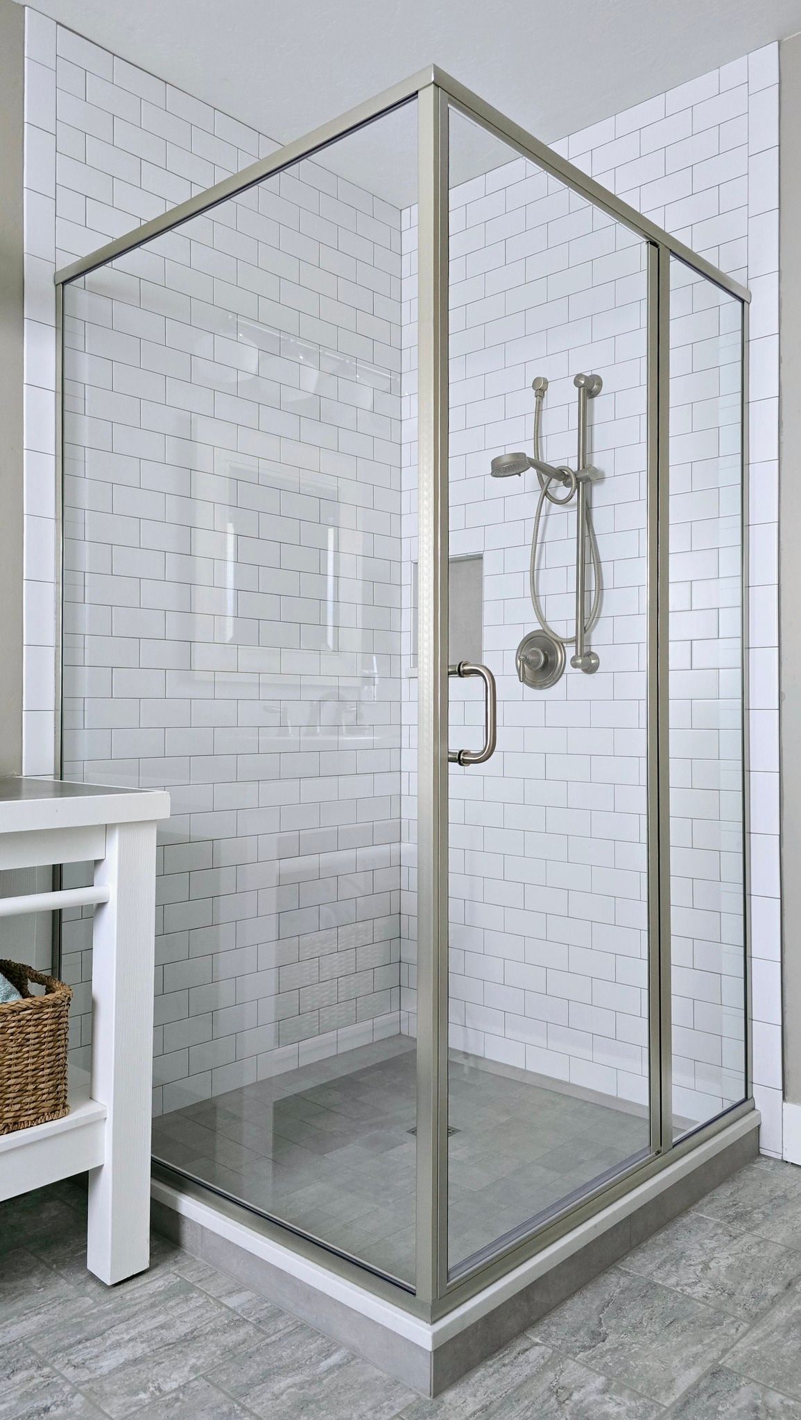 Glass shower with silver fixtures, white tile walls, and a grey floor.