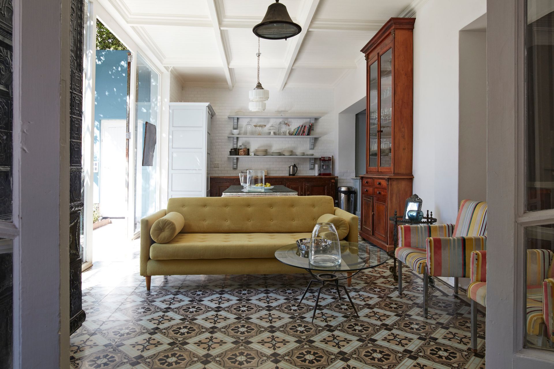 Yellow sofa and patterned tile floor in a bright living space, with a kitchen visible in the background.
