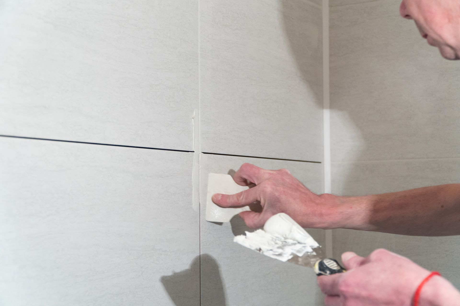 Person applying grout between white tiles with a trowel in a bathroom.