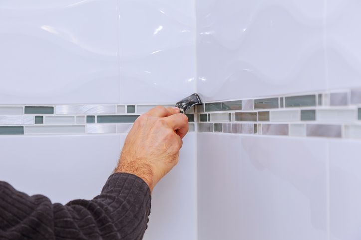 Person using a tool to apply sealant to the corner of a tiled wall.