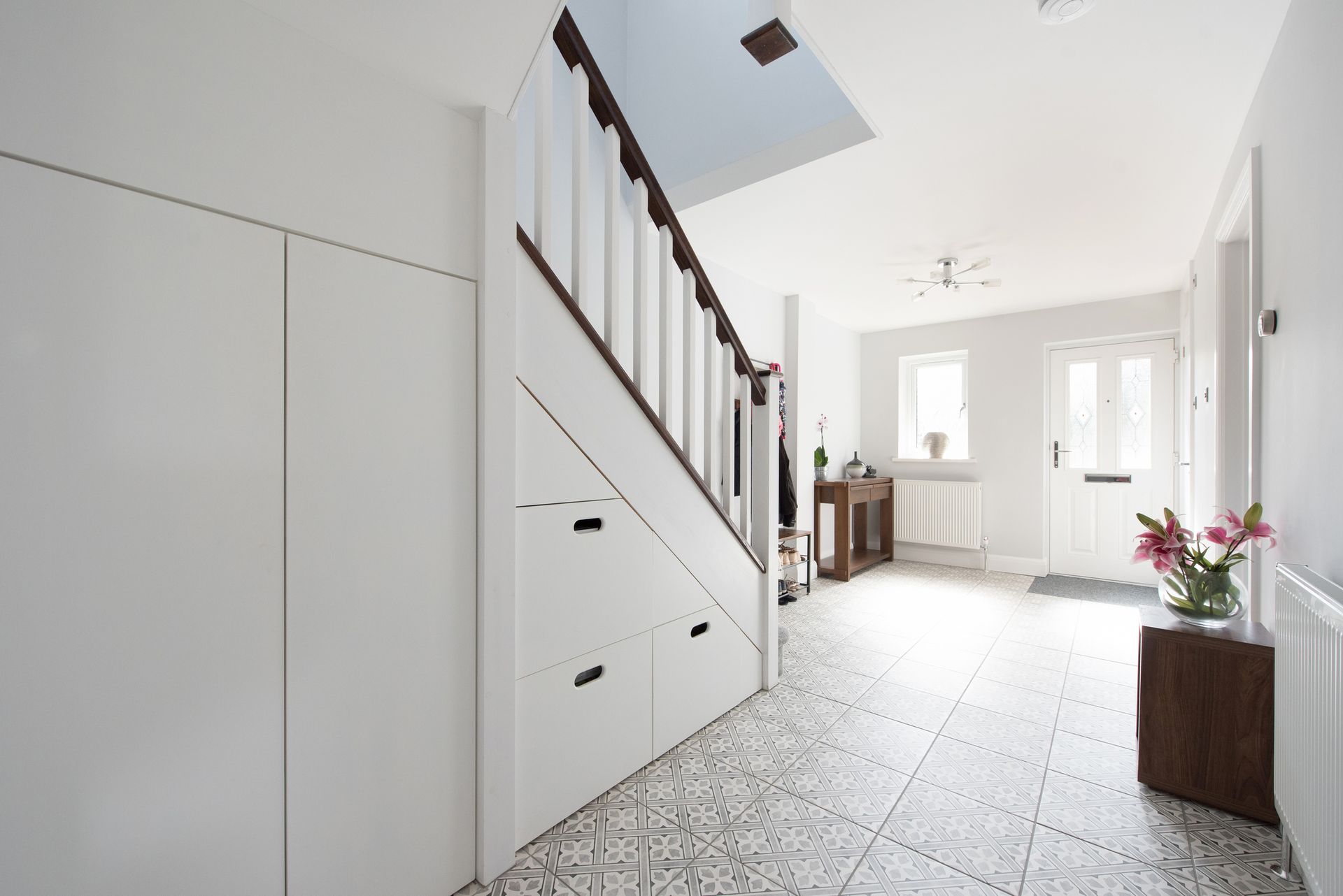 White hallway with stairs and storage. Blue ceiling section, tile floor, and a door at the end.