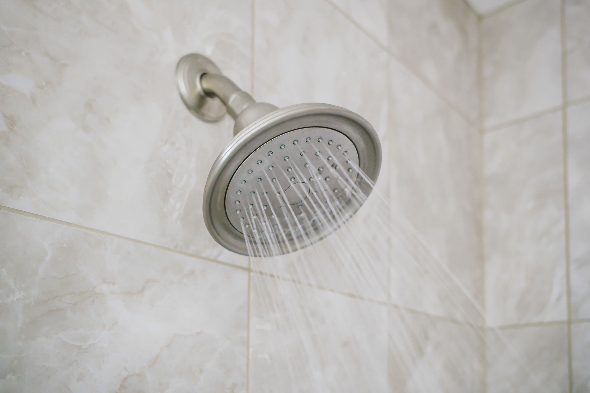 Silver showerhead spraying water against tiled wall.