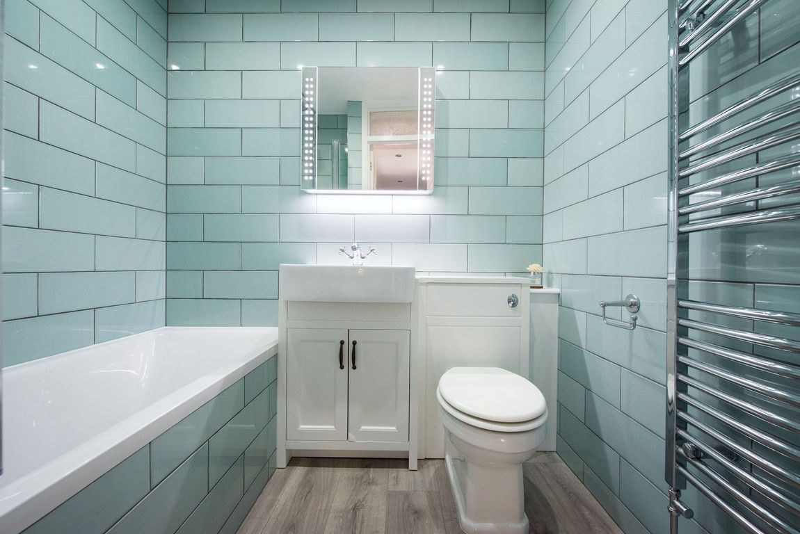 Small bathroom with light blue tiled walls, white fixtures, and a heated towel rack.