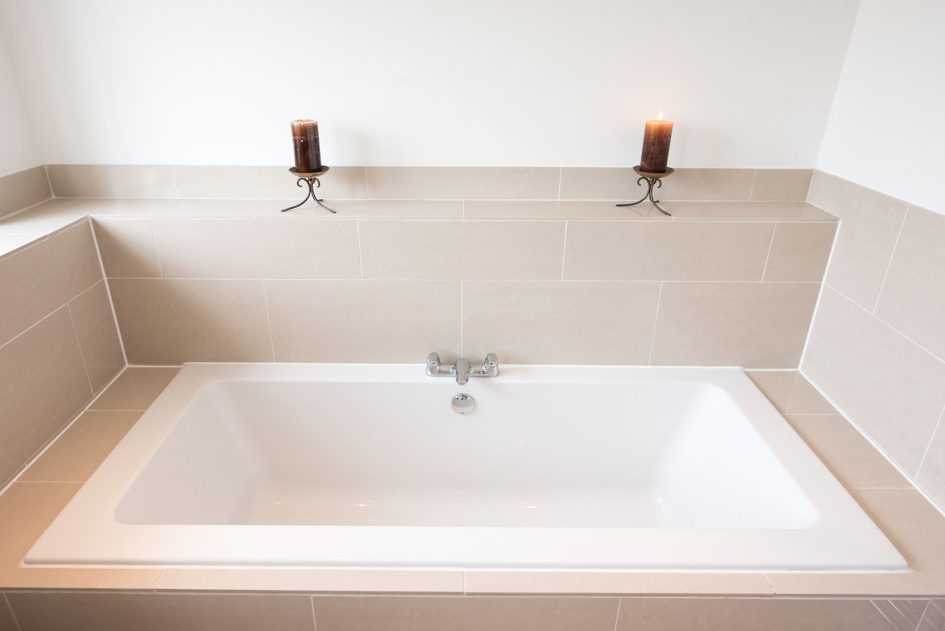White bathtub set in a tiled alcove, with two candle holders mounted above.