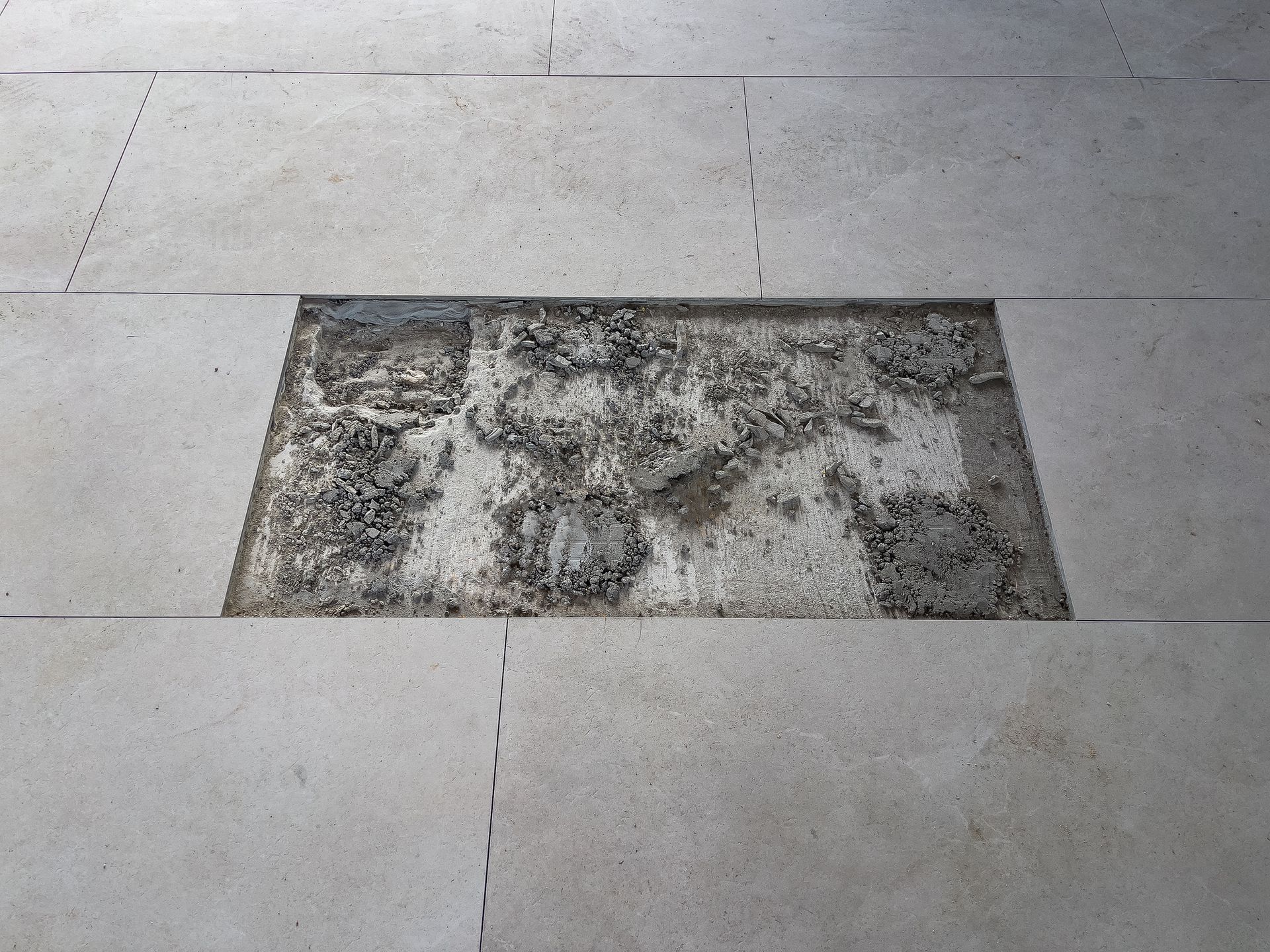 A rectangular inset in light-colored stone paving is filled with rough, gray material.