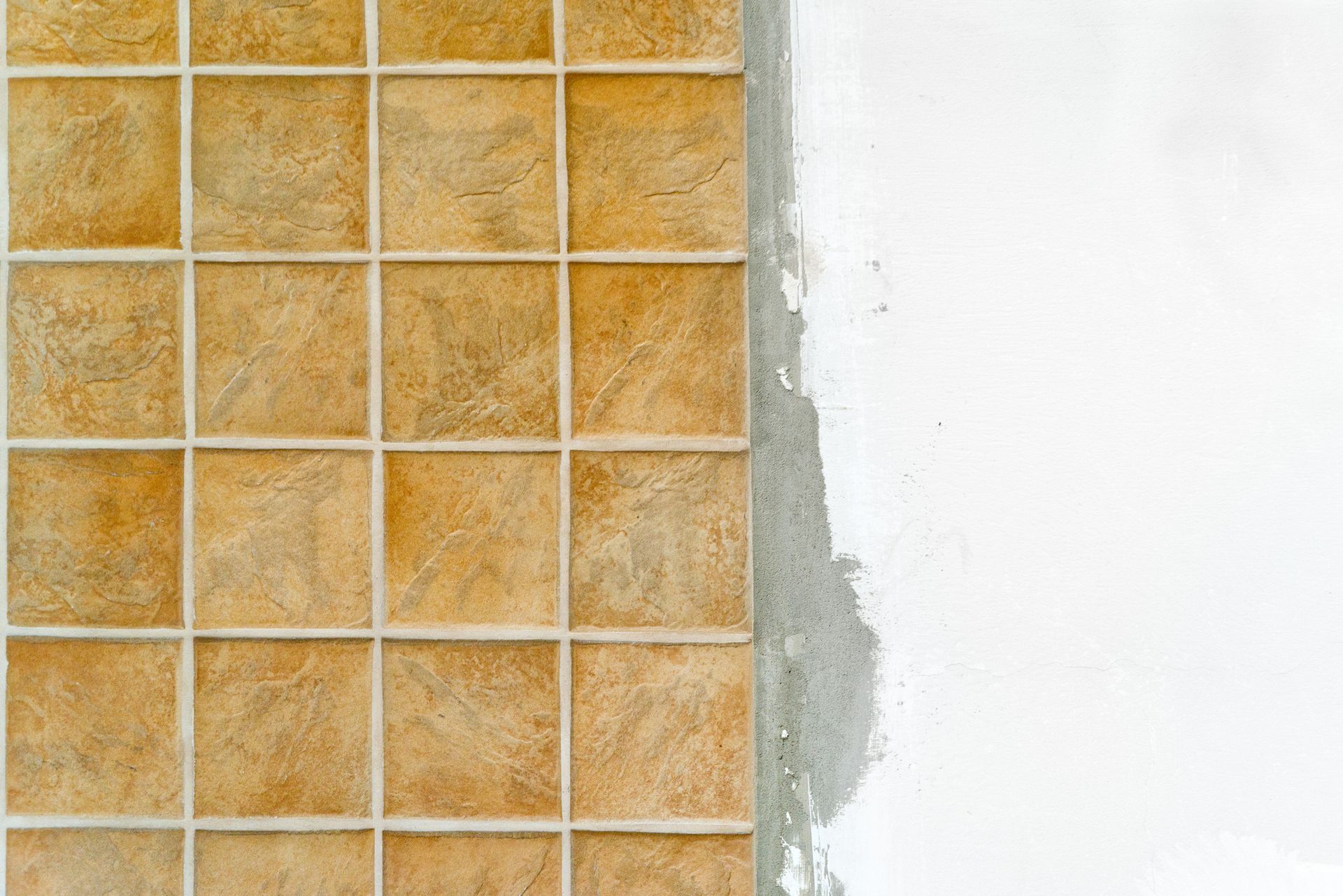 Tile installation in progress: Brown square tiles adjacent to unfinished white wall.