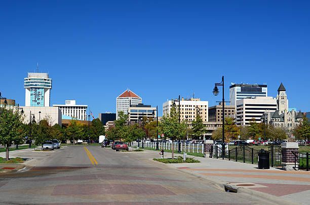 Downtown cityscape with buildings, trees, street, and bright blue sky.